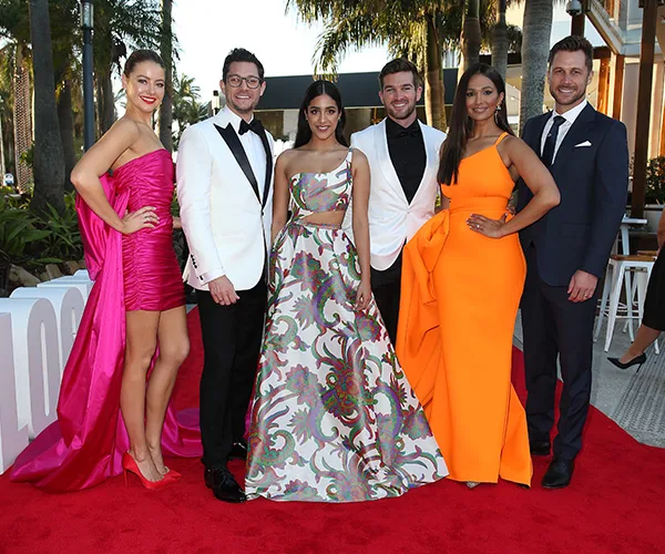 Group of six people in formal attire on the red carpet at the 2019 Logies, outdoors with palm trees in the background.