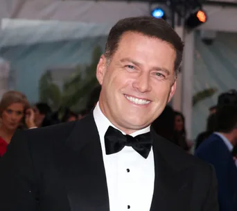 A person in a tuxedo smiling at an event with a crowd in the background.