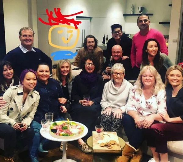 Group of people from Gogglebox together indoors, smiling at the camera, with a drink and snacks on a table.