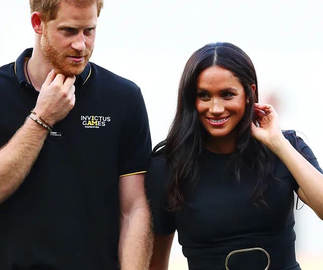 Young couple smiling at an outdoor event; man in black Invictus Games polo, woman in black dress.