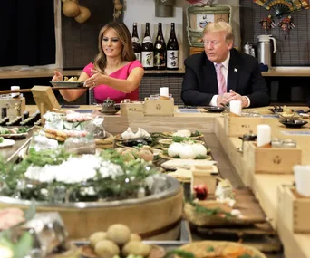 Former First Lady and a man dining at a table with assorted traditional dishes in a Japanese restaurant.