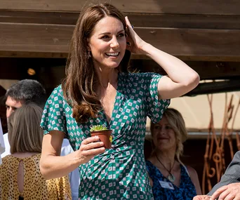 Kate Middleton at Hampton Court Garden, smiling and holding a small plant in a pot, wearing a patterned dress.
