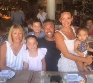 Family smiling at a restaurant table with food and drink in a warm, casual atmosphere.