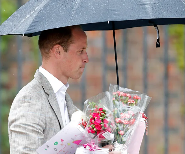 A man holding flowers and cards under an umbrella in the rain.