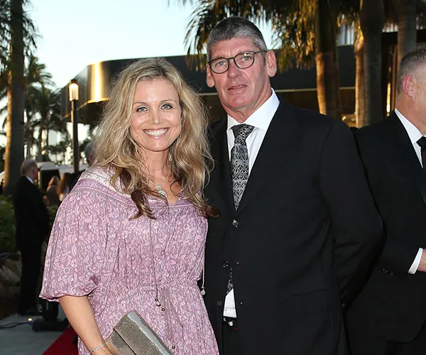 A woman in a pink dress and a man in a suit at an outdoor event, posing for a photo in front of palm trees.