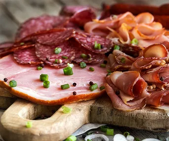 Cured meats on a wooden board, garnished with chopped green onions and peppercorns.
