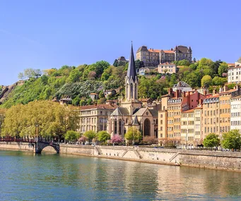 Riverfront view of Lyon, France with colorful buildings and a church spire under a clear blue sky.