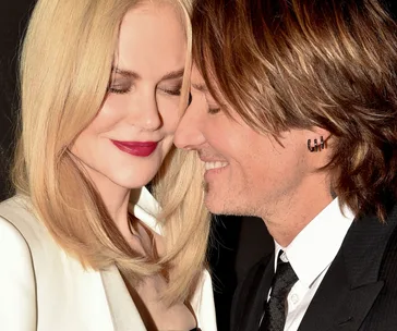 A couple smiling and leaning in close to each other, both with closed eyes and content expressions.