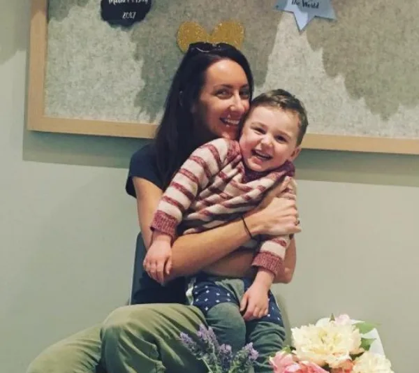 Woman holding a smiling child in a striped sweater, surrounded by flowers indoors.