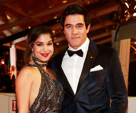 Two people dressed elegantly at an event, with one wearing a sequined dress and the other a tuxedo.