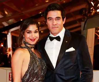 Two people dressed elegantly at an event, with one wearing a sequined dress and the other a tuxedo.