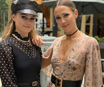 Two women smiling, standing together outdoors with stylish outfits.