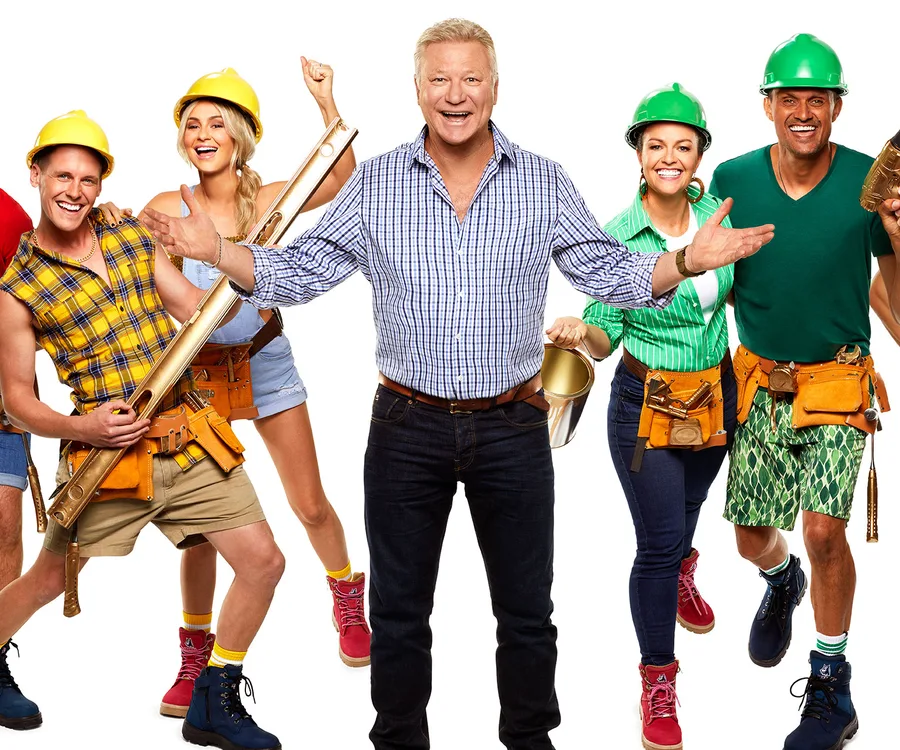 People in construction attire posing energetically; central figure in blue plaid shirt with others in helmets and tool belts.