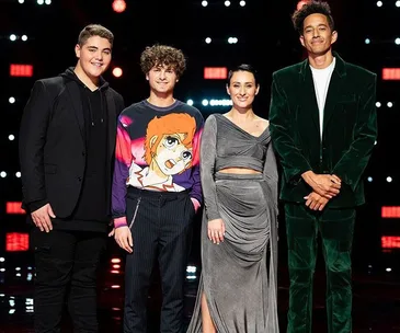 Four "The Voice 2019" finalists stand together on stage, smiling, with colorful lights in the background.