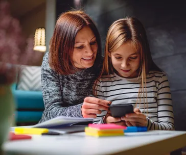 Mother and daughter smiling, looking at a smartphone together in a cozy room.