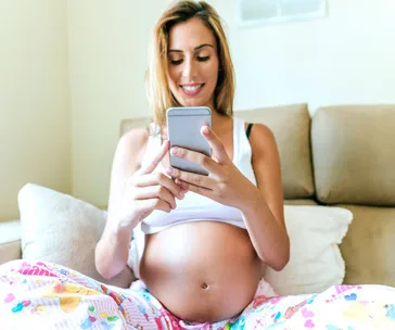 Pregnant woman at 39 weeks sitting on a couch, smiling while using her smartphone.