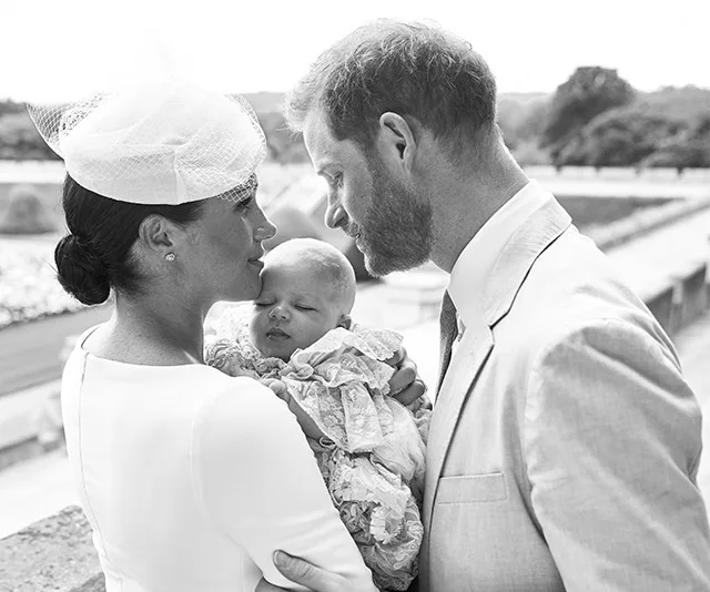 A couple lovingly gazes at their baby wrapped in a lace dress, outdoors on a terrace.