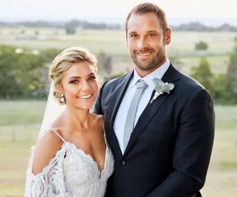 Bride and groom smiling at their wedding, bride in lace dress with veil, groom in suit with boutonniere.