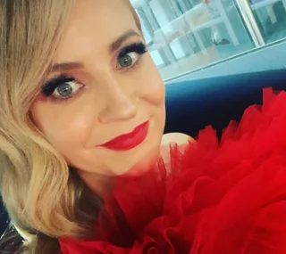 A person with blonde hair and red lipstick smiles, wearing a ruffled red outfit.