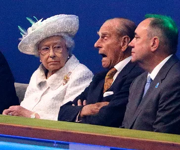 Three elderly individuals sitting together, wearing formal attire, with one speaking animatedly.