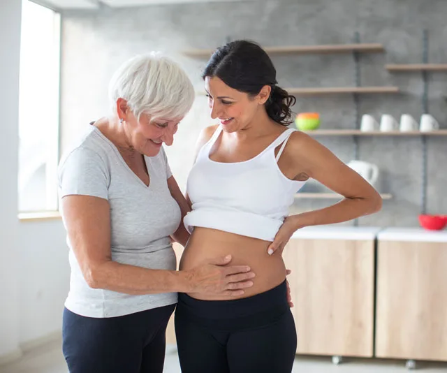 Two women smiling and touching a pregnant belly in a modern kitchen setting.