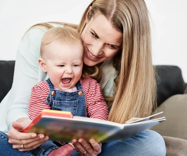 Mother reading a colorful book with a joyful baby on her lap, both smiling and engaged.