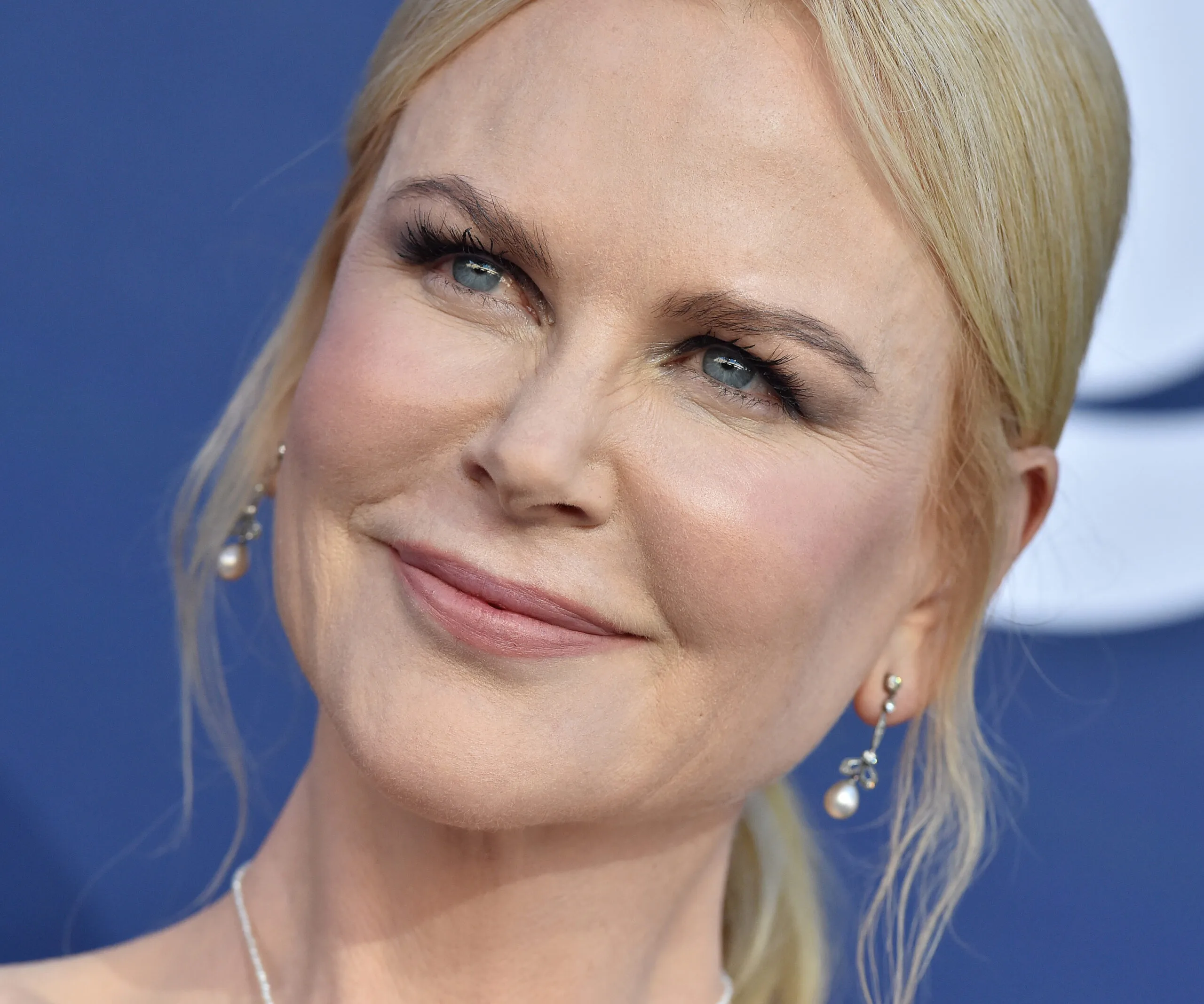 A person with light blonde hair smiling, wearing pearl drop earrings in a close-up shot.