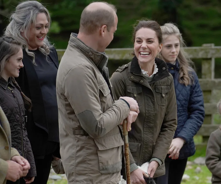 A group of people outdoors, one woman smiling broadly, all wearing jackets and looking engaged in conversation.