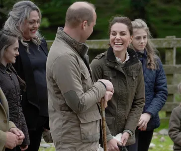 A group of people outdoors, one woman smiling broadly, all wearing jackets and looking engaged in conversation.
