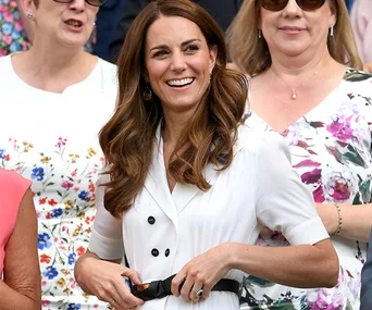 Kate Middleton smiling in a white dress, surrounded by people in floral patterns.
