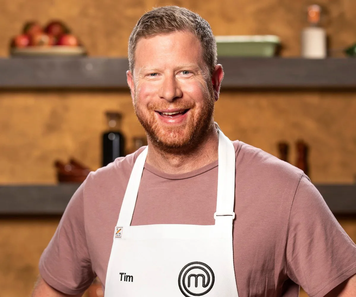 Man in a MasterChef apron smiling in a kitchen setting.