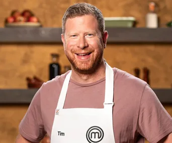 Man in a MasterChef apron smiling in a kitchen setting.