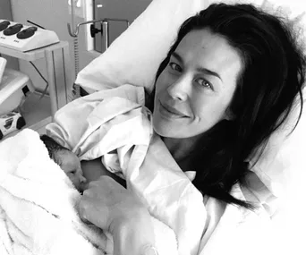 Mother smiling in a hospital bed holding a newborn baby wrapped in a towel.