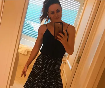 Person taking a mirror selfie in a bathroom wearing a black top and polka dot skirt.