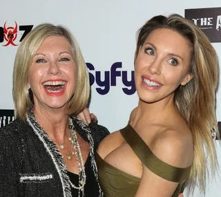 Two women smiling at an event, standing closely together, with logos visible in the background.
