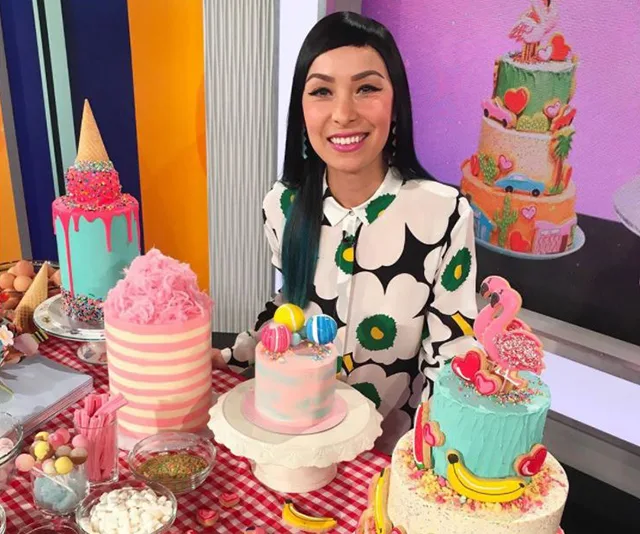 Baker with colorful cakes, including a flamingo and ice cream cone decorations, at a display table with assorted treats.