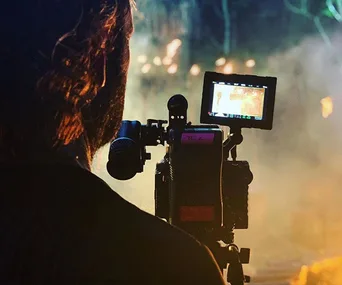 Cameraman filming a scene at night with a dimly lit jungle background on the monitor.