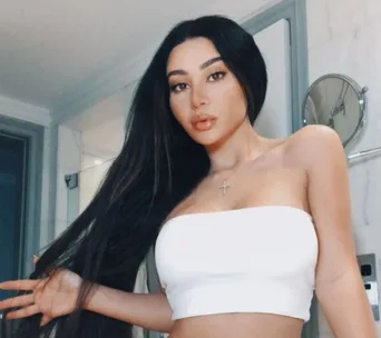 Stylish woman with long hair in a white top, posing indoors.