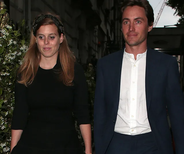 Princess in black dress and man in suit walking on street, evening setting.