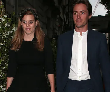 Princess in black dress and man in suit walking on street, evening setting.