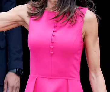 Close-up of a woman in a sleeveless bright pink dress with button details, hair partially visible.