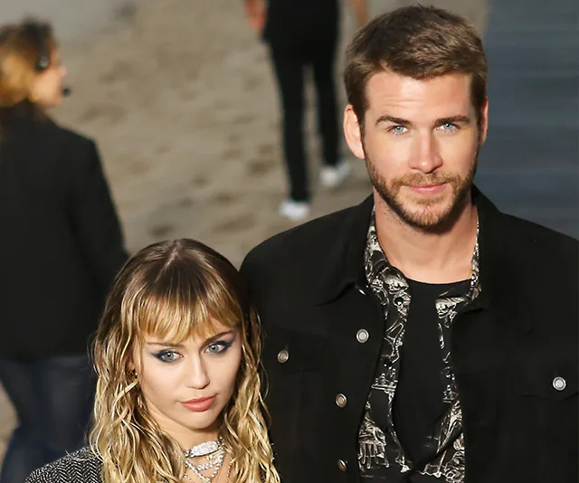 A couple posing together on a red carpet event, with a blurred background of people and a walkway.