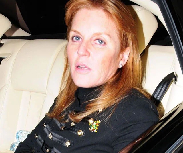 Red-haired woman sitting in a car, wearing a dark top with decorative accents, looking towards the camera.