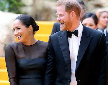 A couple in formal attire, smiling and walking on a yellow carpet at a public event.