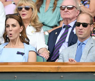 Royals and guests seated at Wimbledon, appearing engaged and wearing summer attire, sunglasses, and expressions of surprise.