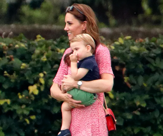Woman in pink dress carrying a young boy in her arms, standing outdoors on a bright day.