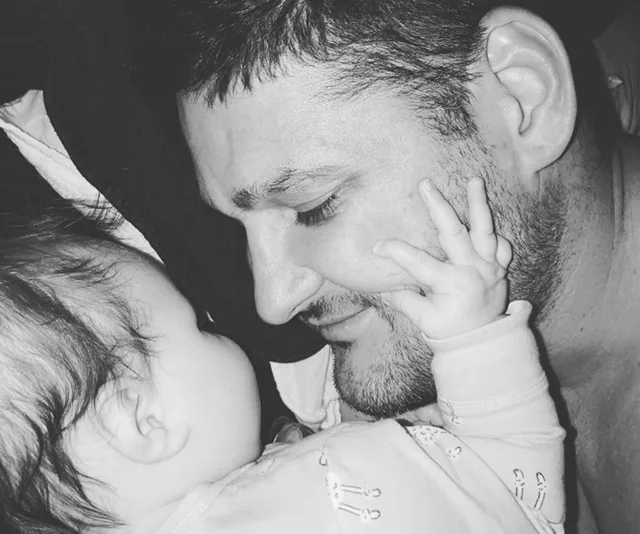 A man and a baby share a tender moment, with the baby touching the man's face.