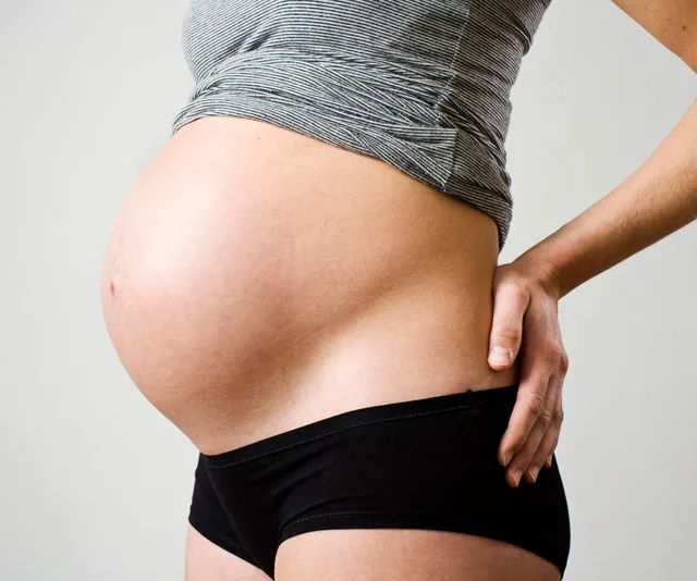 Pregnant woman at 29 weeks in a striped shirt and black underwear, side view of belly.