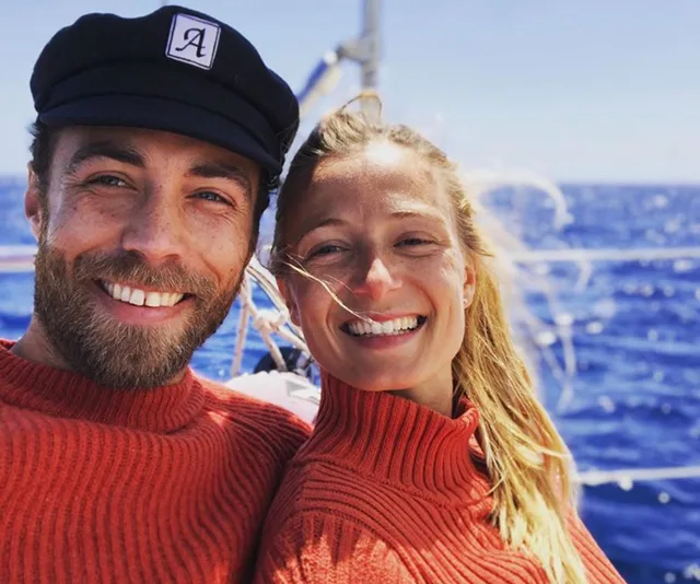 Couple smiling on a boat wearing matching red sweaters with blue sea in background.