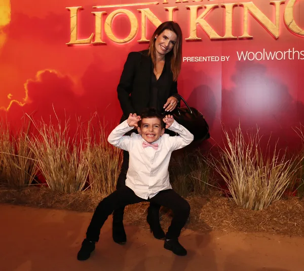 Woman and young boy smiling in front of "Lion King" backdrop with dry grass at their feet.